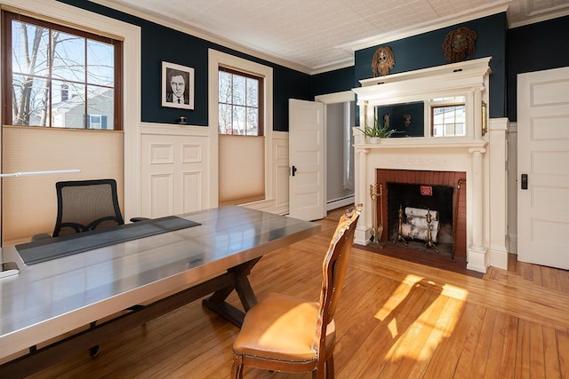 dining space featuring a brick fireplace, crown molding, light wood-type flooring, and baseboard heating