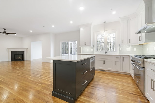 kitchen featuring a kitchen island, pendant lighting, white cabinetry, stainless steel appliances, and wall chimney exhaust hood