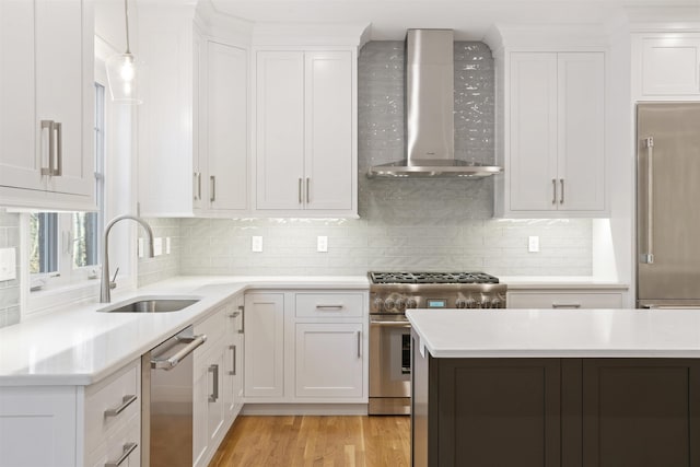 kitchen with wall chimney range hood, sink, light hardwood / wood-style flooring, premium appliances, and white cabinets