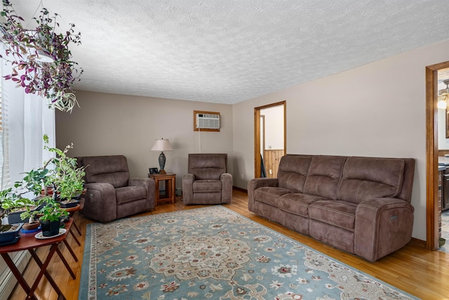 living room with a textured ceiling, a wall unit AC, and light hardwood / wood-style flooring