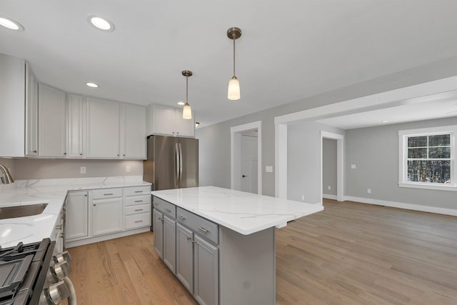 kitchen featuring pendant lighting, sink, appliances with stainless steel finishes, a center island, and light stone countertops