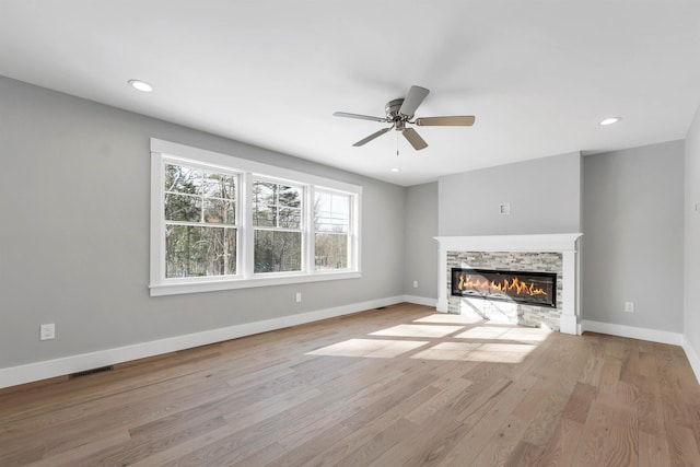 unfurnished living room featuring ceiling fan, a stone fireplace, and light hardwood / wood-style floors