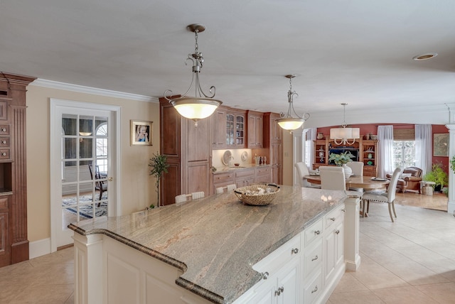 kitchen with pendant lighting, light stone counters, ornamental molding, white cabinets, and light tile patterned flooring