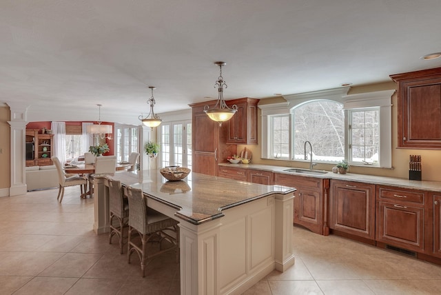 kitchen featuring sink, hanging light fixtures, a kitchen breakfast bar, a center island, and light stone counters