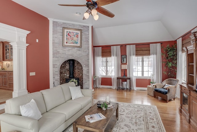 living room with ornate columns, ceiling fan, light hardwood / wood-style flooring, and a wood stove