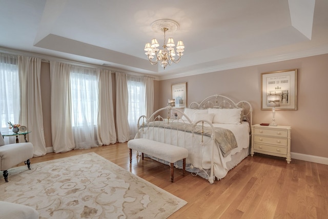 bedroom with crown molding, light hardwood / wood-style flooring, a chandelier, and a tray ceiling