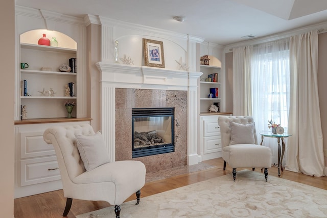 sitting room featuring built in shelves, ornamental molding, a premium fireplace, and light wood-type flooring