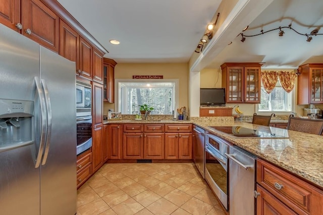 kitchen featuring light tile patterned floors, light stone counters, stainless steel appliances, a sink, and brown cabinetry