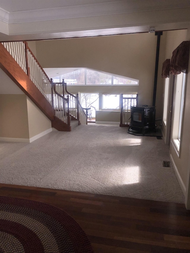 unfurnished living room featuring visible vents, stairway, ornamental molding, a wood stove, and baseboards