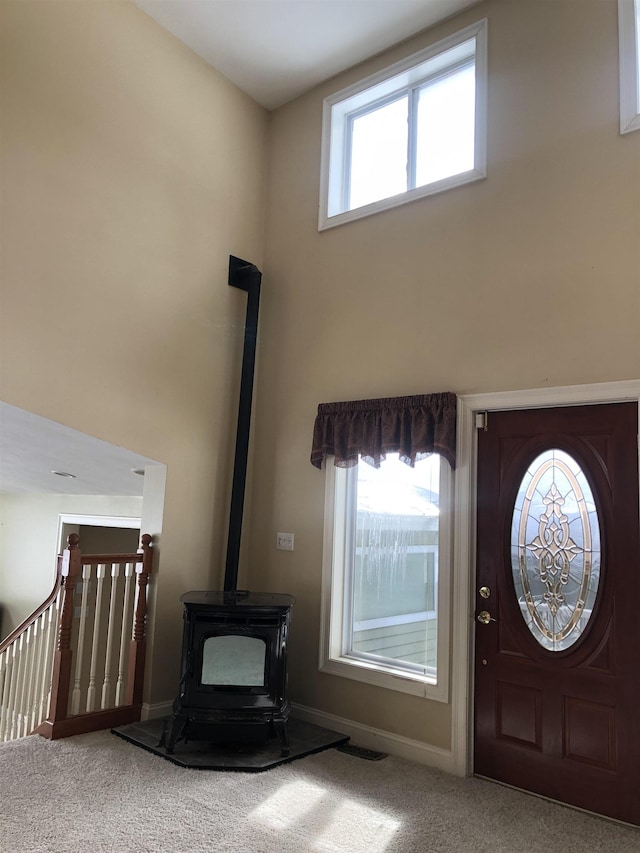 entryway with baseboards, visible vents, a wood stove, carpet, and a high ceiling