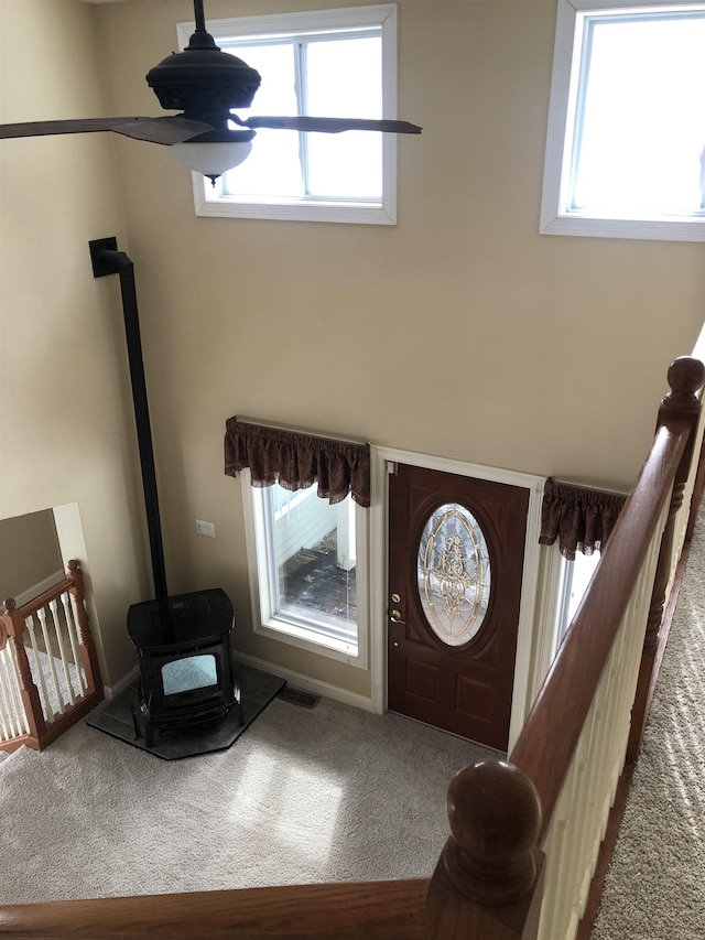 carpeted foyer entrance featuring a wood stove, visible vents, plenty of natural light, and baseboards