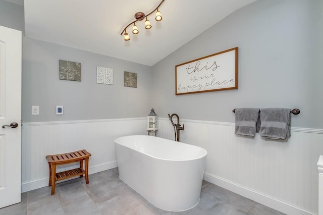 full bathroom with lofted ceiling, a freestanding tub, and wainscoting