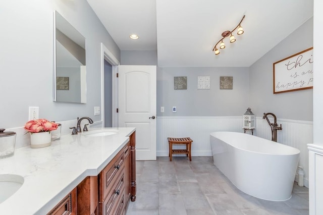 full bath featuring double vanity, a freestanding tub, a sink, and wainscoting