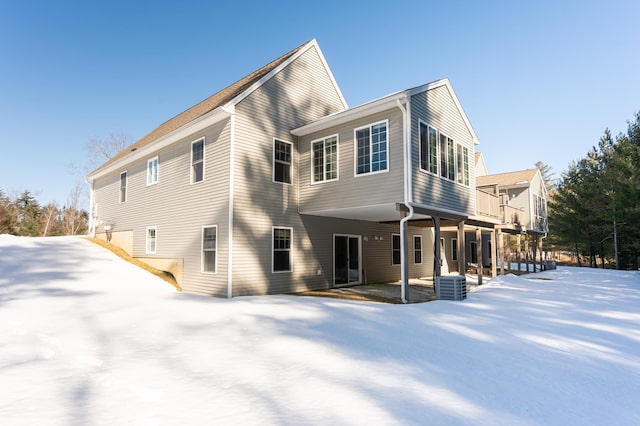 snow covered back of property with a balcony and central AC unit