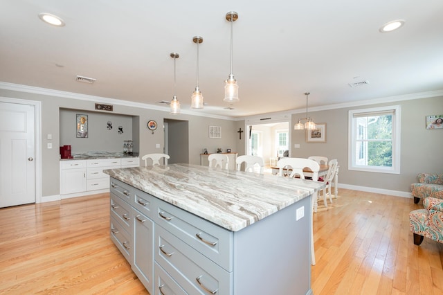 kitchen featuring a kitchen island, decorative light fixtures, light stone counters, crown molding, and light hardwood / wood-style flooring