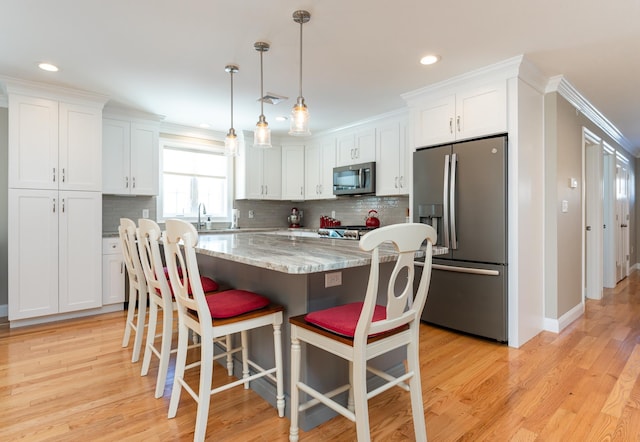 kitchen featuring appliances with stainless steel finishes, white cabinetry, a kitchen bar, hanging light fixtures, and a center island