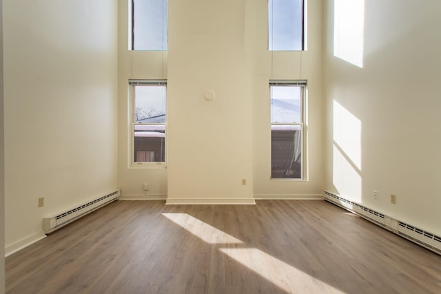 unfurnished room with a baseboard radiator, light hardwood / wood-style flooring, and a high ceiling