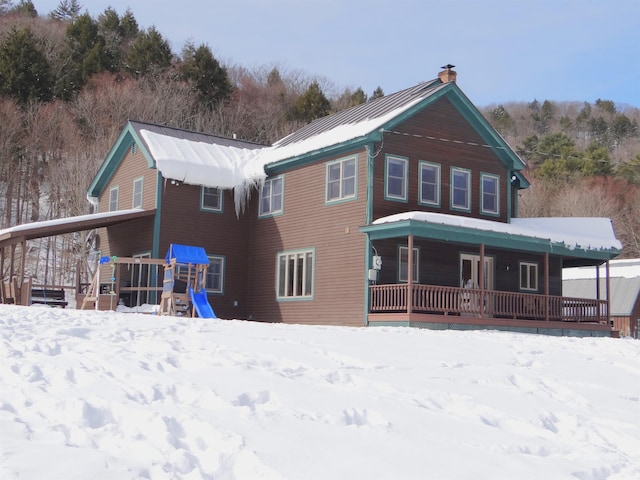 snow covered house featuring a playground and a porch