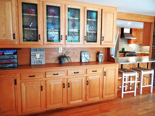 bar featuring tasteful backsplash, stainless steel refrigerator, wall chimney range hood, light hardwood / wood-style floors, and stove