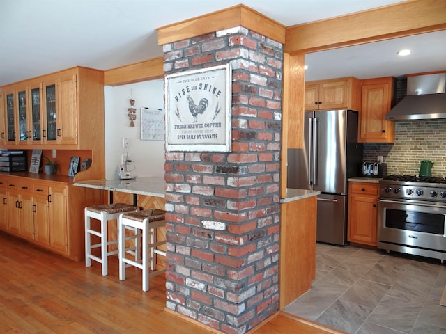 kitchen featuring wall chimney range hood, appliances with stainless steel finishes, a kitchen breakfast bar, decorative backsplash, and kitchen peninsula