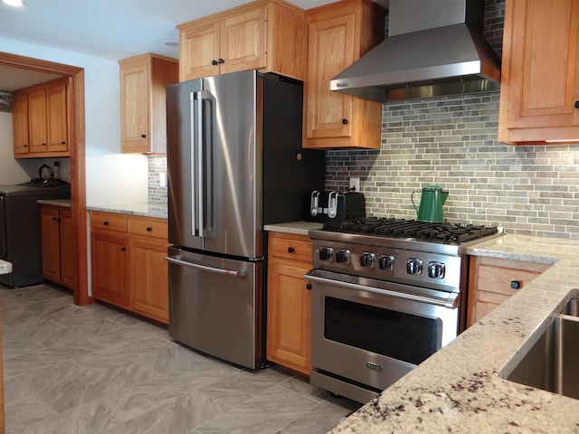 kitchen featuring appliances with stainless steel finishes, separate washer and dryer, decorative backsplash, light stone counters, and wall chimney range hood