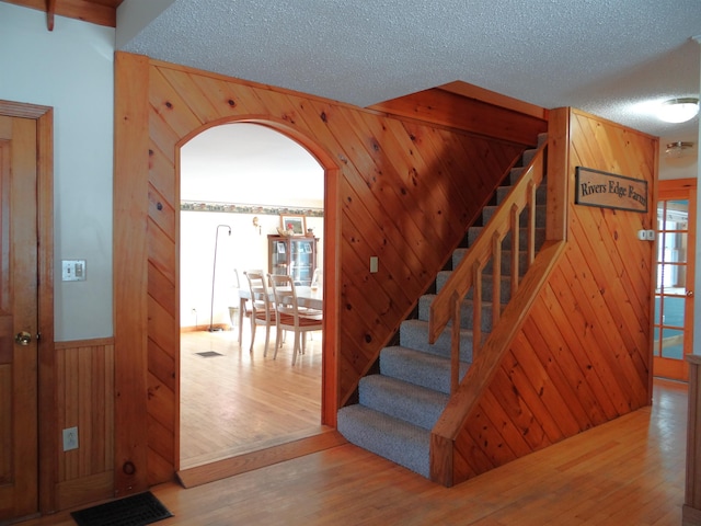 staircase featuring wooden walls, hardwood / wood-style floors, and a textured ceiling