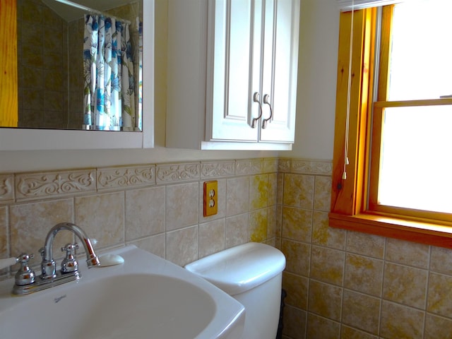 bathroom with toilet, curtained shower, sink, and tile walls