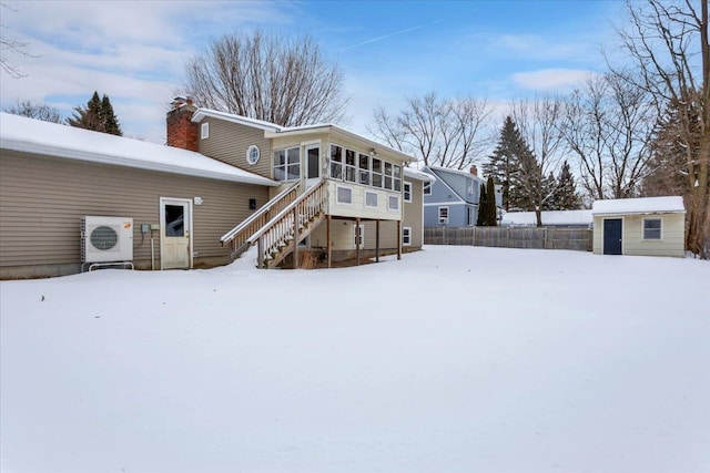 snow covered back of property with a sunroom, a shed, and ac unit