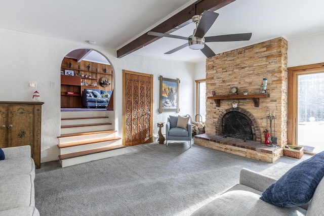 living room with ceiling fan, a large fireplace, beam ceiling, and carpet flooring