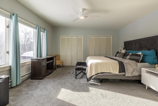 carpeted bedroom featuring baseboard heating, ceiling fan, and two closets