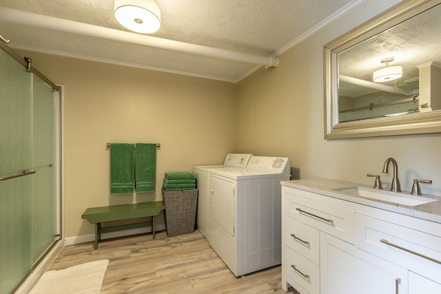 washroom featuring sink, crown molding, a textured ceiling, washing machine and clothes dryer, and light wood-type flooring