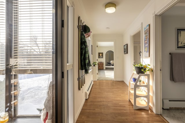 corridor with ornamental molding, a baseboard heating unit, and hardwood / wood-style floors