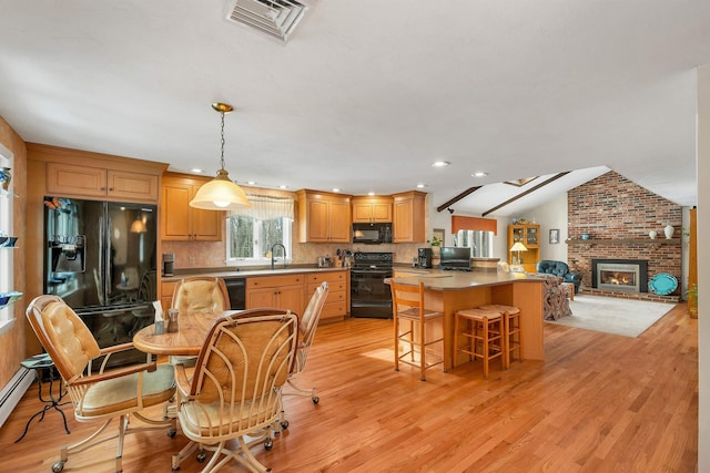 kitchen with a breakfast bar, lofted ceiling, sink, black appliances, and light wood-type flooring