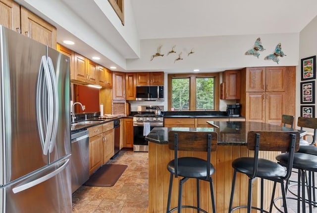 kitchen with appliances with stainless steel finishes, sink, a kitchen bar, dark stone counters, and a center island