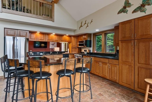 kitchen with appliances with stainless steel finishes, high vaulted ceiling, sink, a breakfast bar area, and a center island