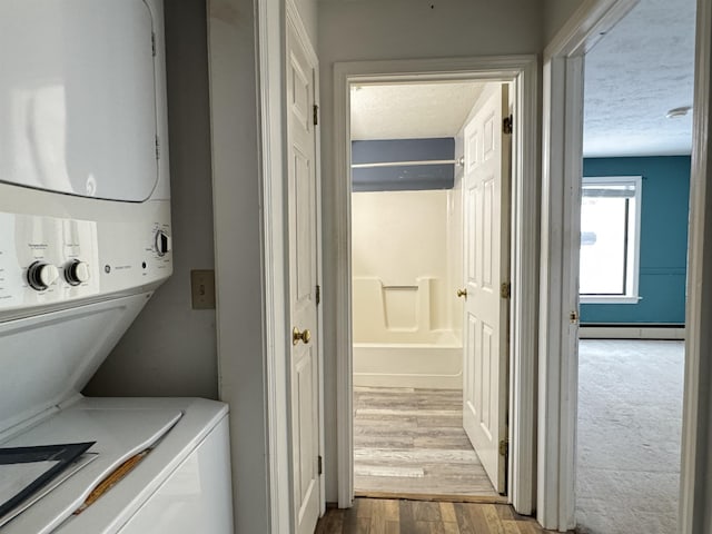 washroom featuring a textured ceiling, light hardwood / wood-style floors, a baseboard radiator, and stacked washer and clothes dryer