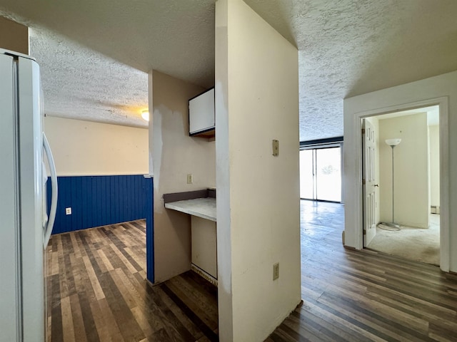 corridor with dark wood-type flooring, a baseboard heating unit, and a textured ceiling