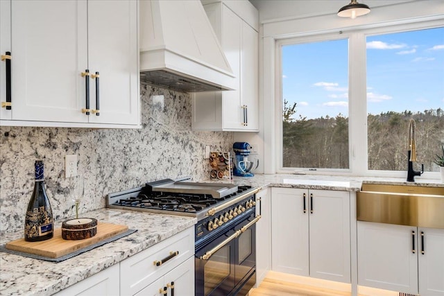kitchen featuring custom exhaust hood, backsplash, white cabinets, and range with two ovens