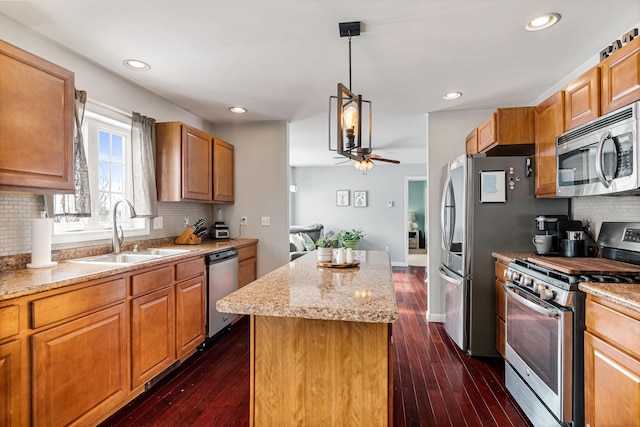 kitchen featuring appliances with stainless steel finishes, a ceiling fan, dark wood-type flooring, a sink, and a kitchen island