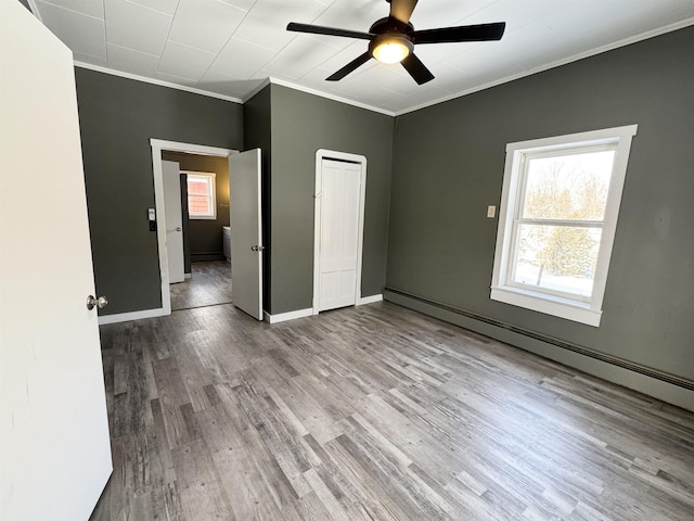 unfurnished bedroom featuring crown molding, ceiling fan, baseboard heating, a closet, and light wood-type flooring