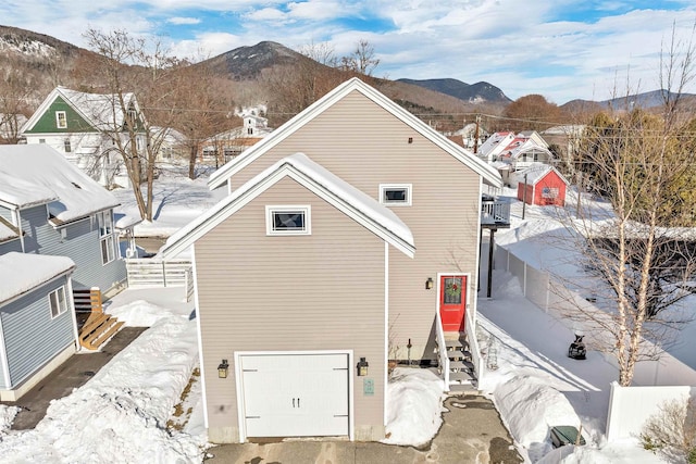 snow covered back of property featuring a garage and a mountain view