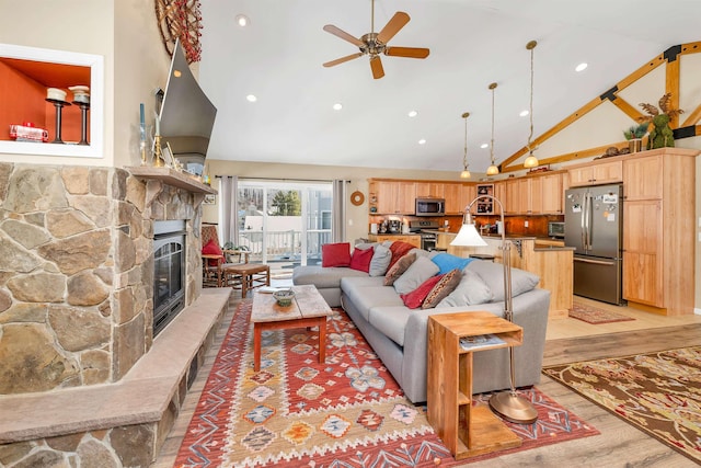 living room with ceiling fan, a stone fireplace, high vaulted ceiling, and light hardwood / wood-style floors