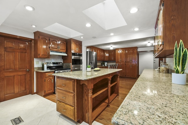 kitchen featuring a skylight, stainless steel appliances, light stone counters, a kitchen island, and decorative backsplash