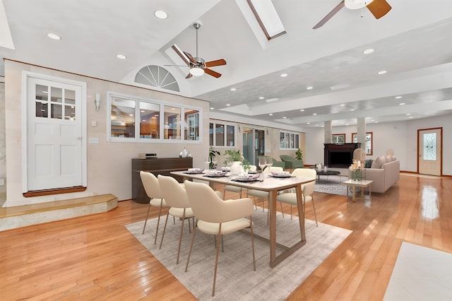 dining room with ceiling fan, vaulted ceiling with skylight, and light hardwood / wood-style floors