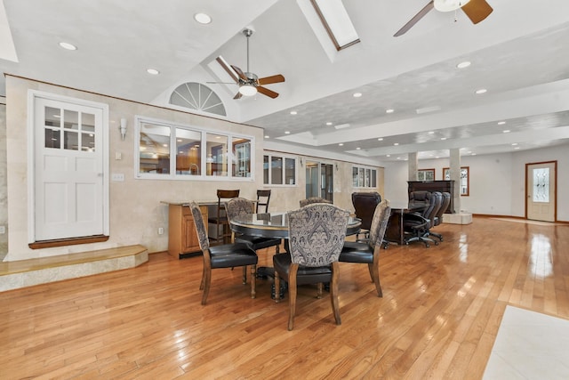 dining space with ceiling fan, vaulted ceiling with skylight, and light hardwood / wood-style flooring