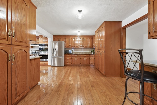 kitchen featuring light stone counters, light hardwood / wood-style flooring, stainless steel appliances, and a textured ceiling