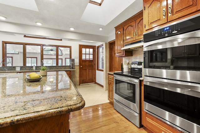 kitchen featuring light stone counters, a skylight, light hardwood / wood-style flooring, appliances with stainless steel finishes, and decorative backsplash