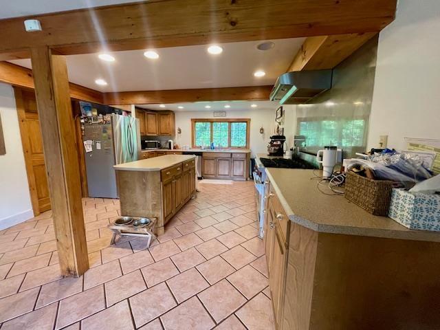 kitchen featuring a kitchen island, appliances with stainless steel finishes, light tile patterned floors, and beam ceiling