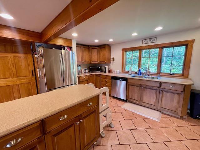 kitchen featuring light tile patterned flooring, appliances with stainless steel finishes, beam ceiling, and sink