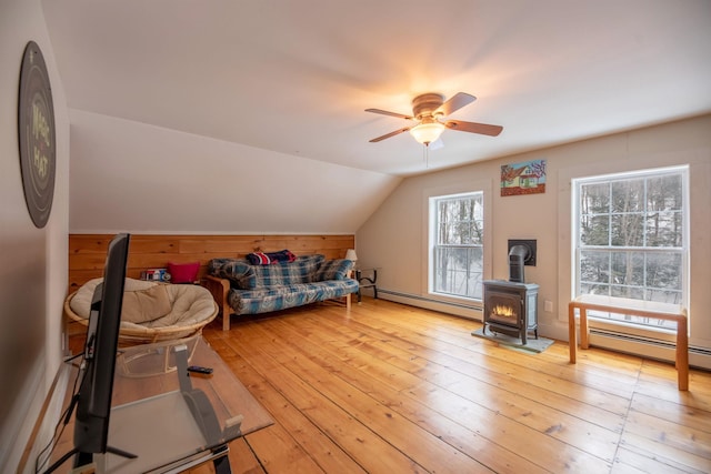 interior space with vaulted ceiling, a baseboard heating unit, a wood stove, and light hardwood / wood-style flooring